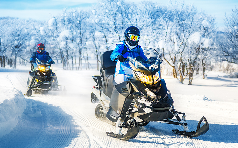 Two people riding snowmobiles on a groomed trail.